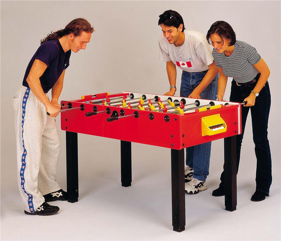 Drei Personen spielen gemeinsam an einem roten Tischfußballtisch und lachen dabei.