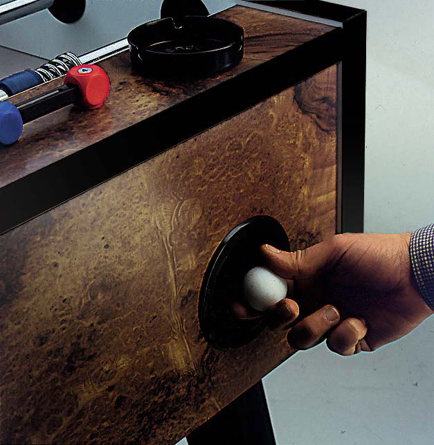 Hand dreht den Griff eines Tischfußballspiels, während zwei Spielfiguren auf der Spielfläche sichtbar sind.