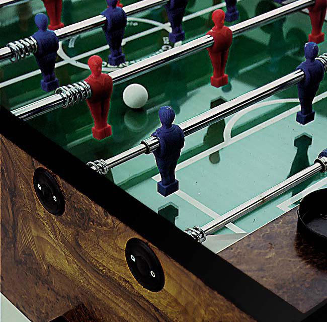 Tischfußballspiel mit roten und blauen Spielfiguren auf grünem Spielfeld, weiße Kugel in der Mitte.
