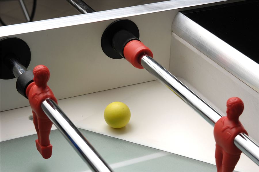 Tischkicker-Spielfiguren in Rot mit gelbem Ball auf dem Spielfeld.